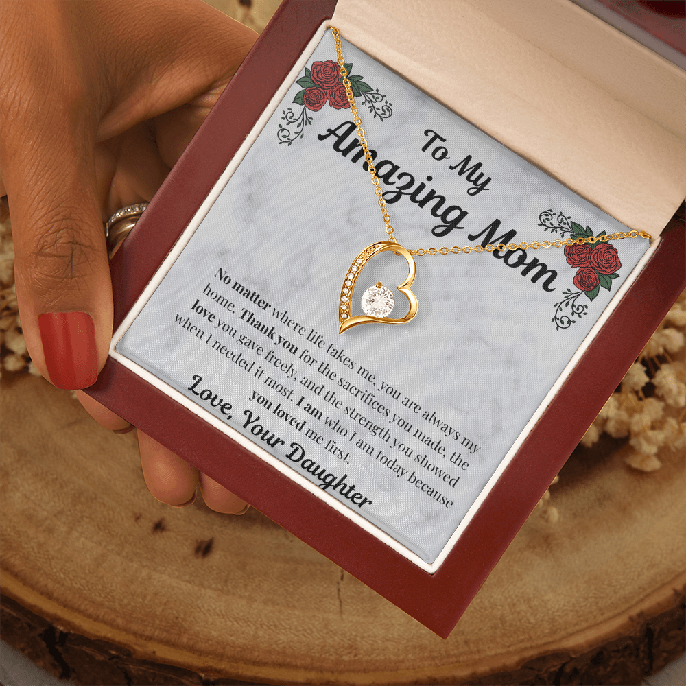 Hand holding 18k yellow gold-finish Forever Love Necklace in mahogany gift box on wooden table