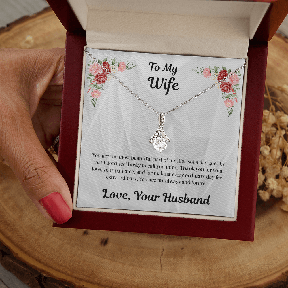 Hand holding 14k white gold-finish Alluring Beauty Necklace in mahogany gift box on wooden table