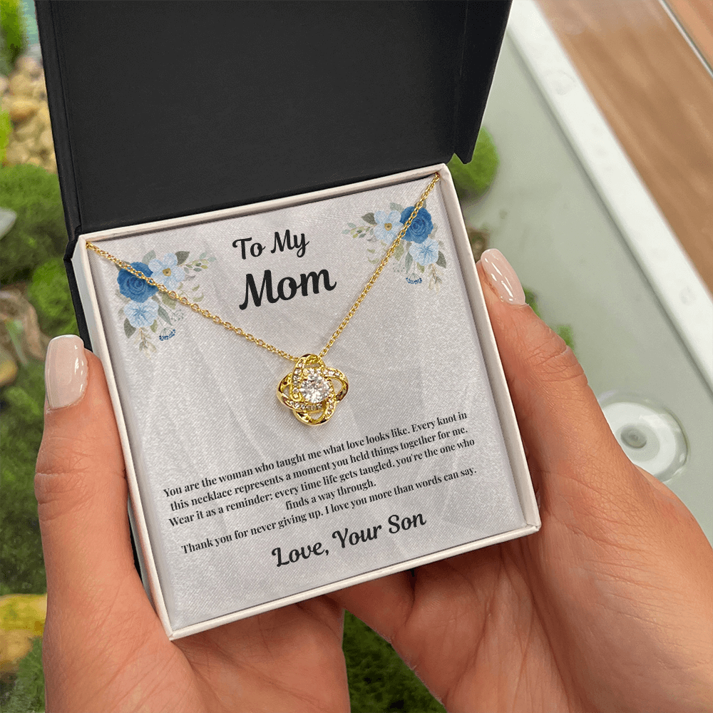Hand holding 18K yellow gold-finish Love Knot Necklace in standard gift box outdoors