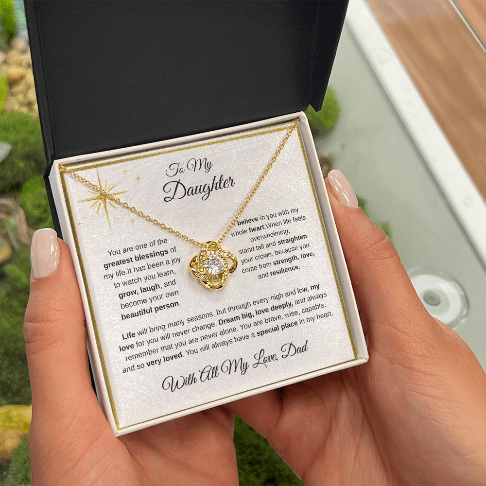 Hand holding 18K yellow gold-finish Love Knot Necklace in standard gift box outdoors