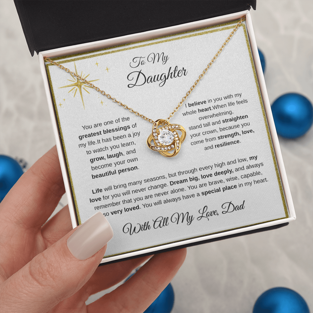 Hand holding 18K yellow gold-finish Love Knot Necklace in standard gift box with blue ornaments