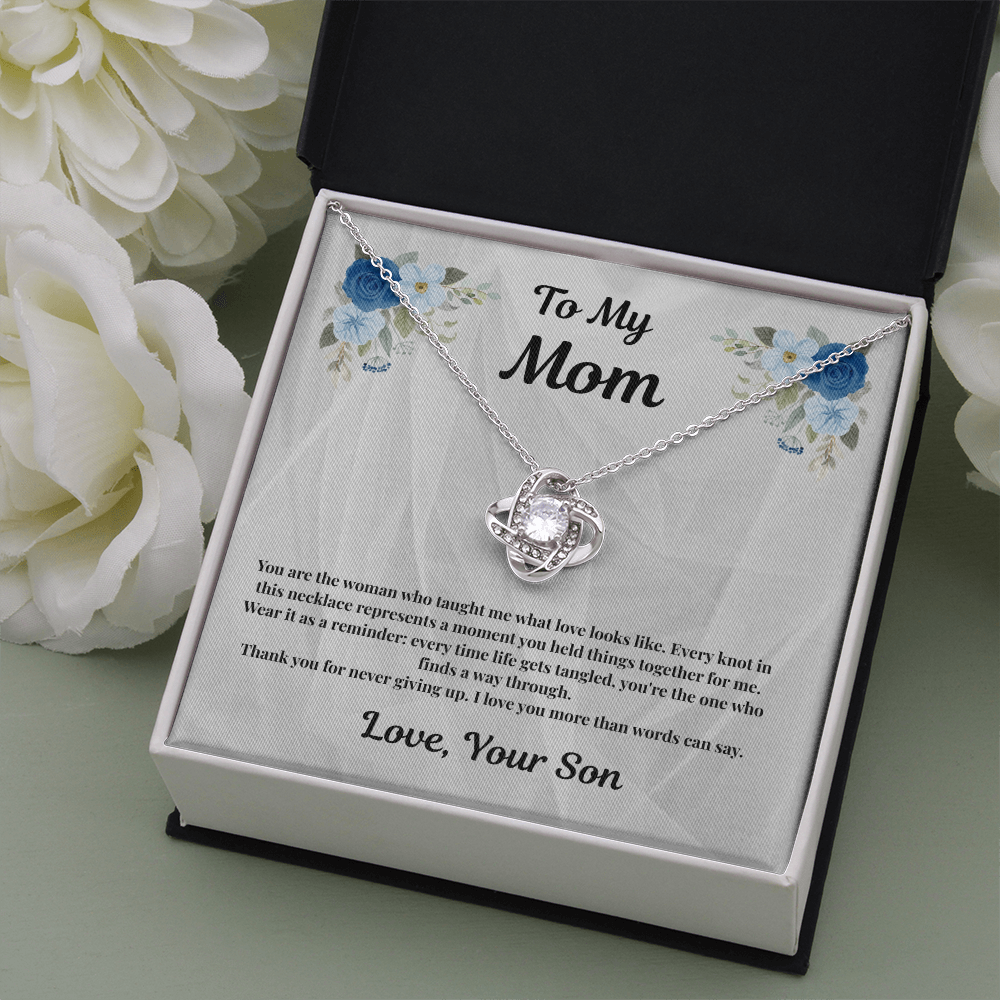 14K white gold-finish Love Knot Necklace in standard gift box beside white flowers
