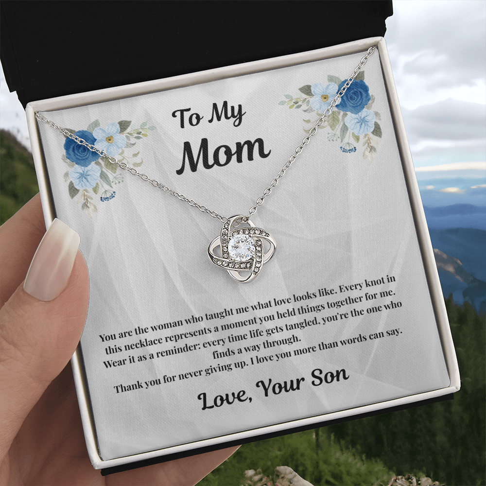Hand holding 14K white gold-finish Love Knot Necklace in standard gift box outdoors