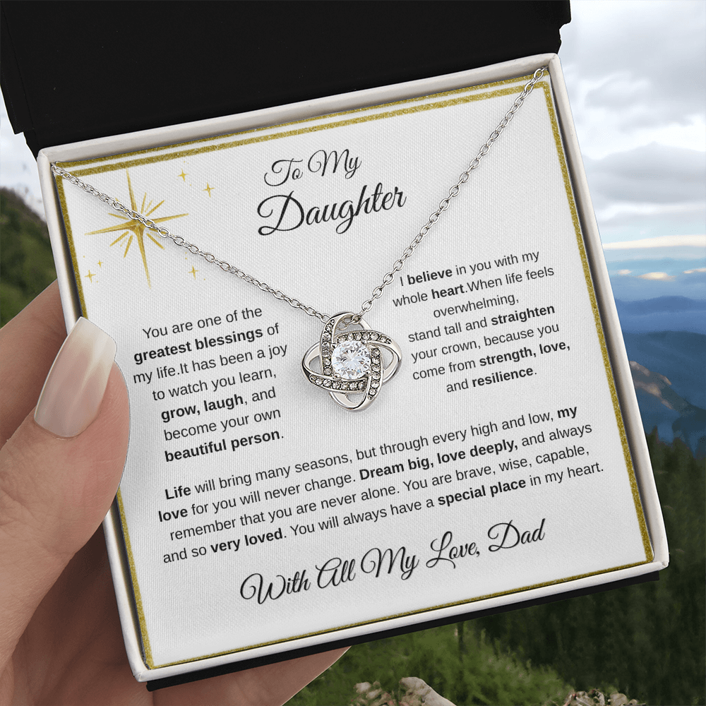 Hand holding 14K white gold-finish Love Knot Necklace in standard gift box outdoors