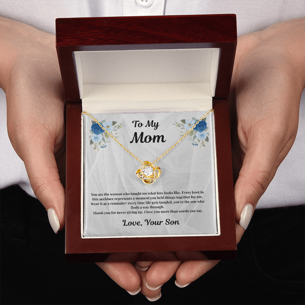 Hands holding 18K yellow gold-finish Love Knot Necklace in mahogany gift box