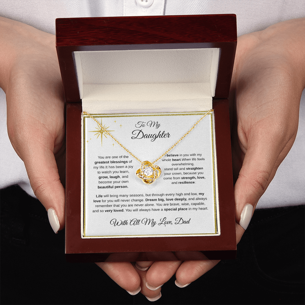 Two hands holding 18K yellow gold-finish Love Knot Necklace in mahogany gift box