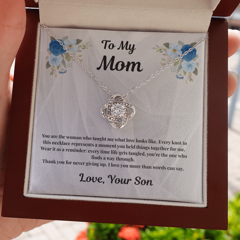 Hand holding 14K white gold-finish Love Knot Necklace in mahogany gift box outdoors