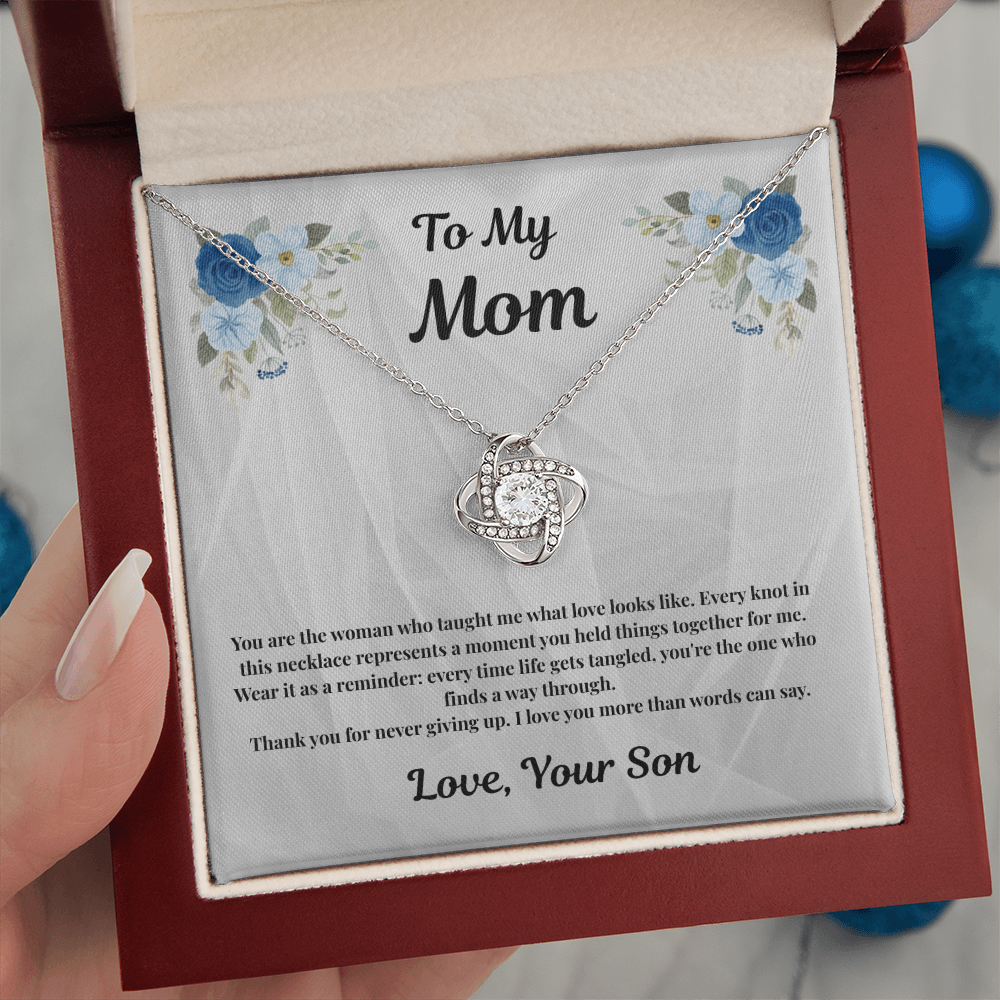 Hand holding 14K white gold-finish Love Knot Necklace in mahogany gift box indoors