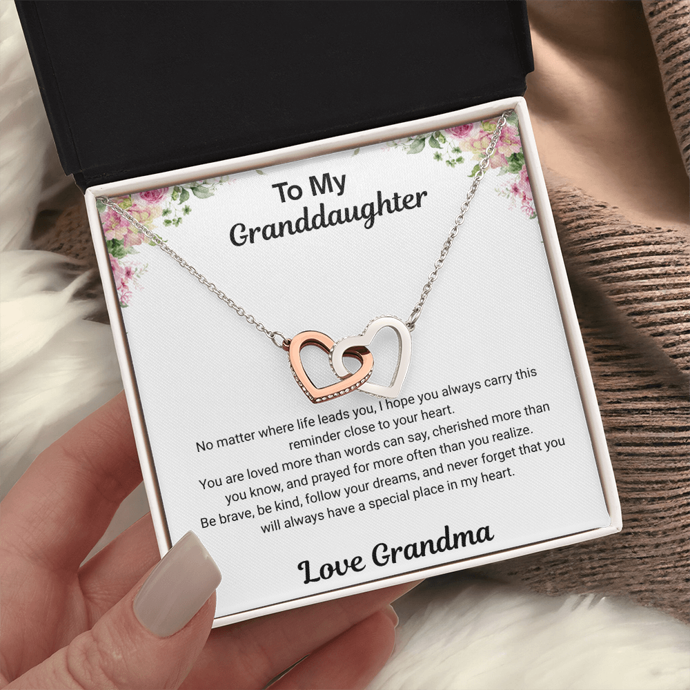 Hand holding 14k white gold-finish Interlocking Hearts Necklace in standard gift box with To My Granddaughter message card from Grandma on soft fabric background
