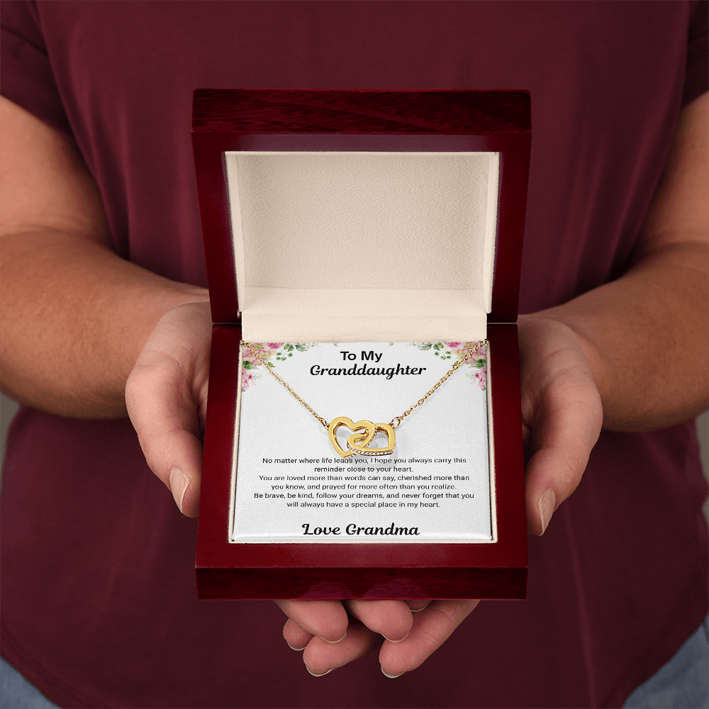 Hands holding 18k yellow gold-finish Interlocking Hearts Necklace in open mahogany-style luxury box with To My Granddaughter message card from Grandma
