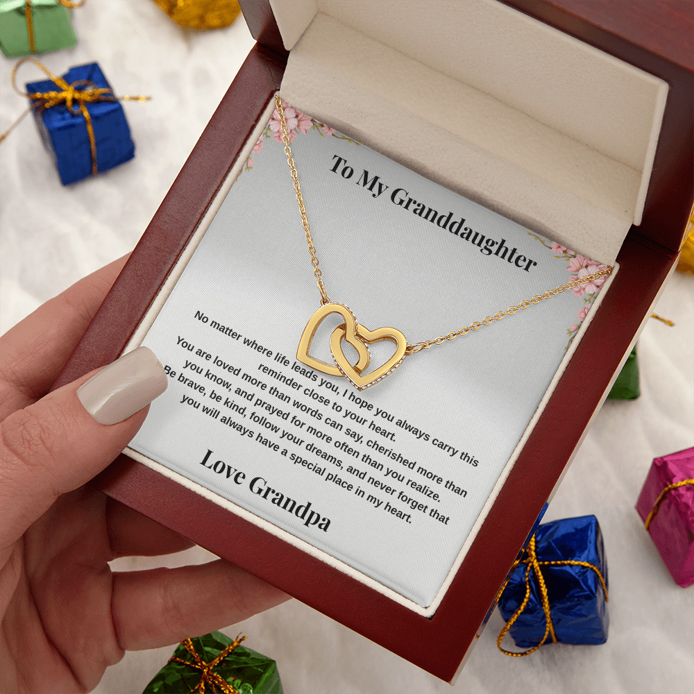 Hand holding 18k yellow gold-finish Interlocking Hearts Necklace in open mahogany-style luxury box with To My Granddaughter message card and gift boxes in background