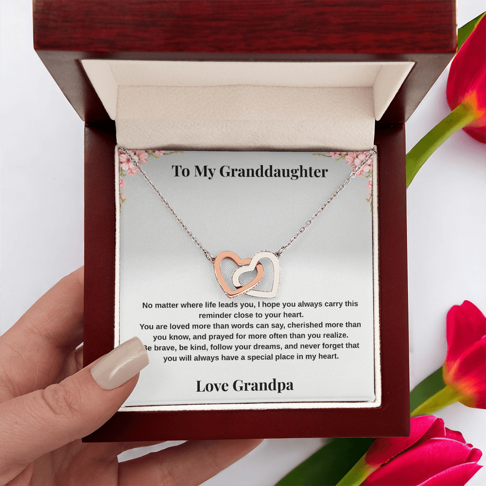 Hand holding 14k white gold-finish Interlocking Hearts Necklace in mahogany-style luxury box with To My Granddaughter message card and red flowers