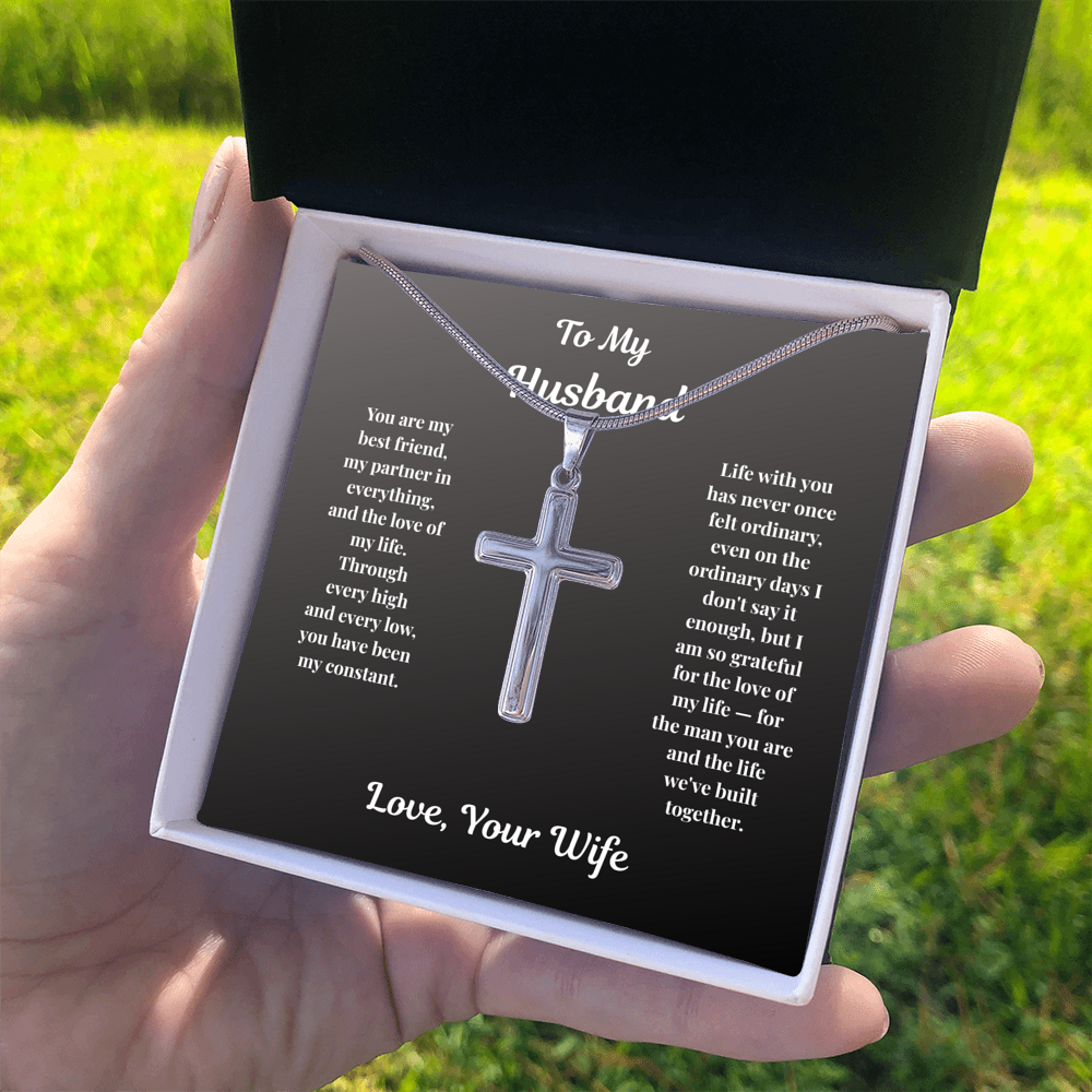 Hand holding stainless steel Cross Necklace in standard gift box outdoors