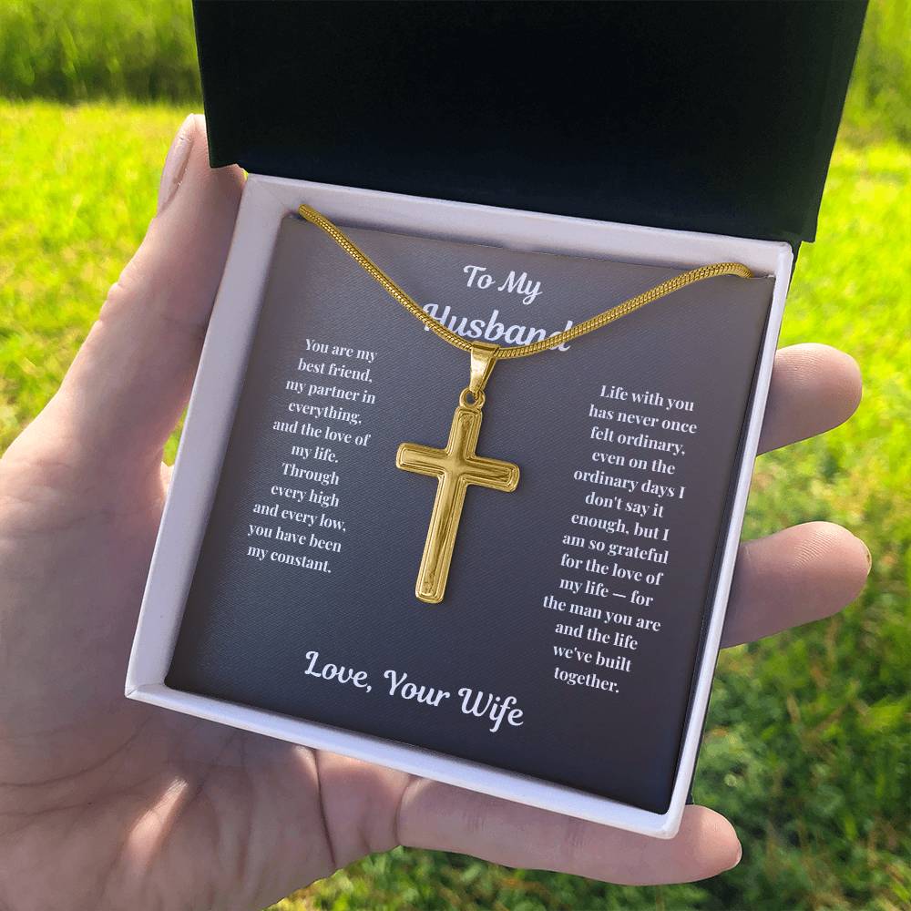 Hand holding gold-finish Cross Necklace in standard gift box outdoors